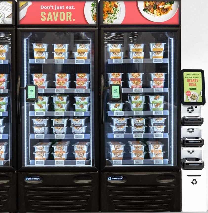 Smart Fridge™ cabinets stocked with chef-prepared meals beside a stack of Smart Cooker™ units