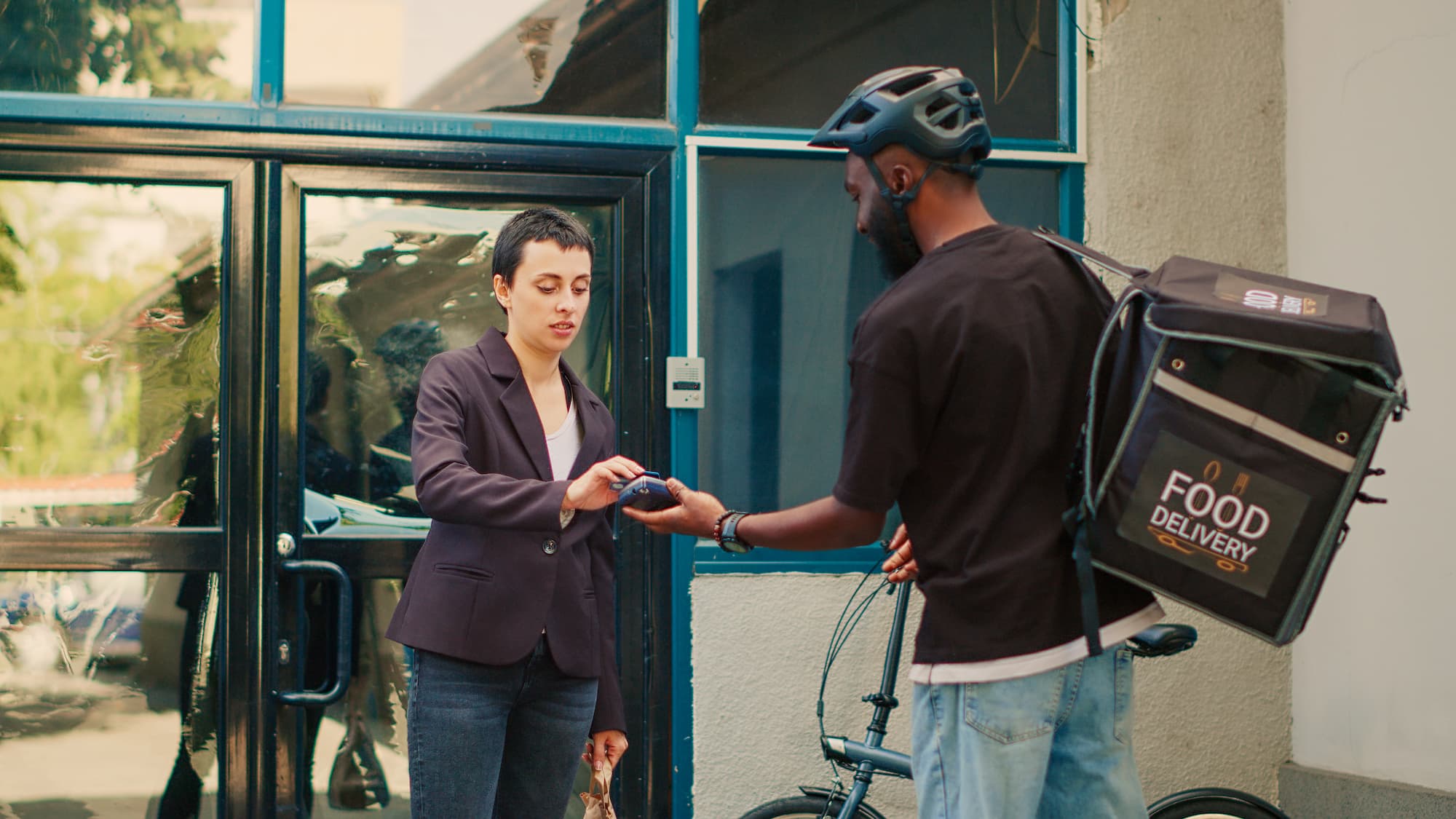 An office worker paying a food delivery courier outside a building entrance